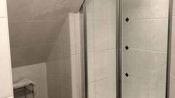 A shower with a glass door, white tiled walls, and a wooden floor.