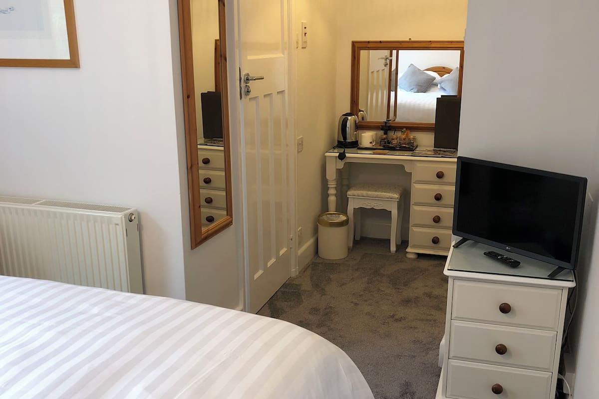 A bedroom with a bed, a dresser, a television, and a bathroom visible through an open door.