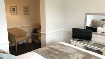 Una habitación de hotel con cama, una silla, escritorio con lámpara, televisor y espejo.