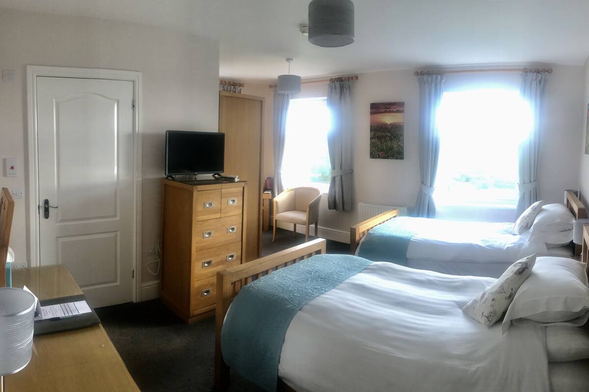 A hotel room with two beds, a wooden dresser, a television, and a desk with a chair.