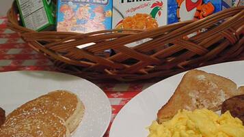 Una escena de desayuno con platos de comida, una cesta con cajas de cereales y un mantel a cuadros.