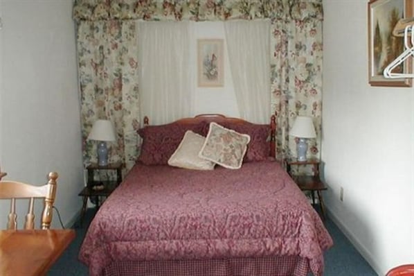 A bedroom with a floral-patterned canopy bed, two bedside lamps, and a wooden chair.