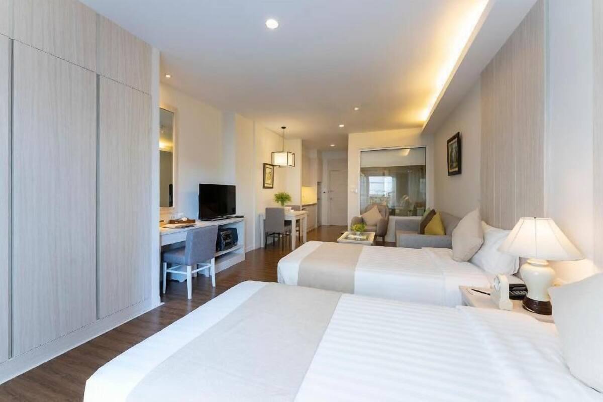 A hotel room with two beds, a desk, a chair, a TV, and a lamp.