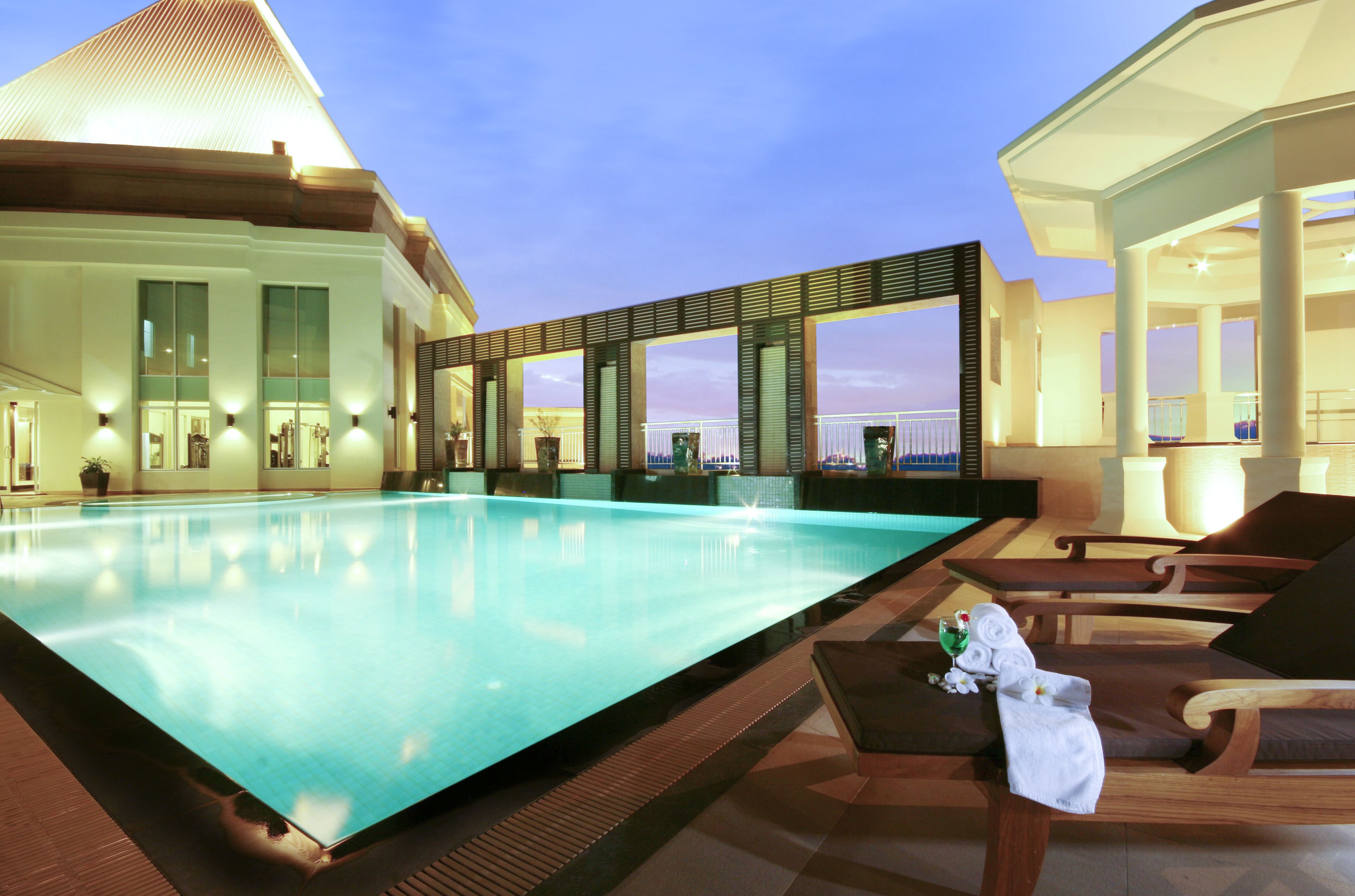 Una piscina infinita en la azotea con sillones de descanso y vistas al horizonte urbano.