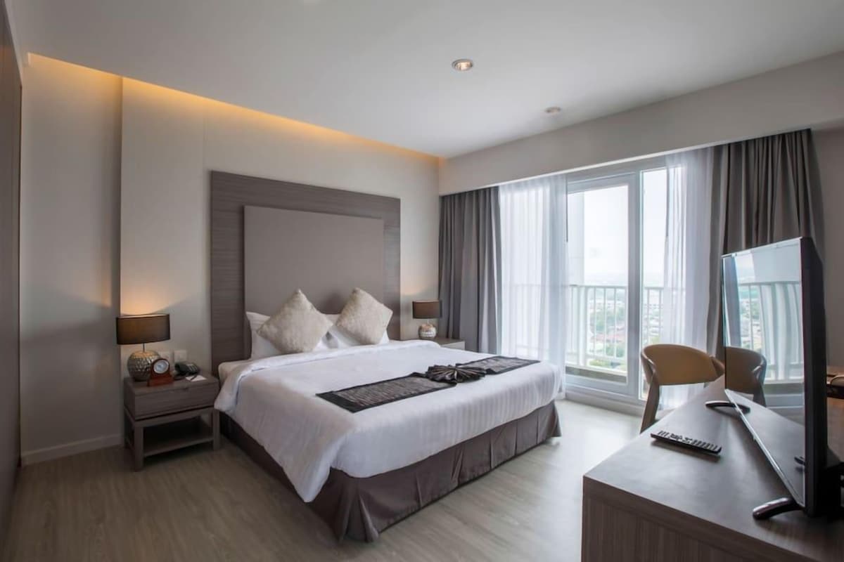 A modern hotel room with a large bed, a desk, and a TV.