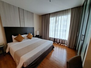 A hotel room with a large bed, a nightstand, a chair, and a window with curtains.