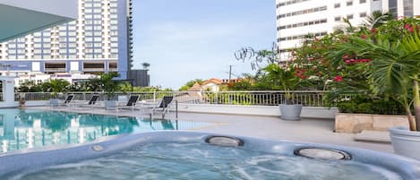 A swimming pool with hot tubs, surrounded by tall buildings and potted plants.