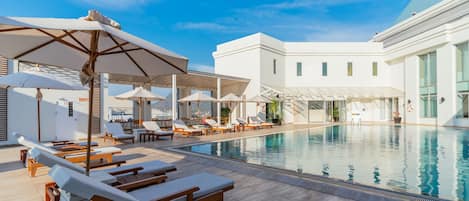 A poolside area with sun loungers and umbrellas, a clear blue sky, and a modern building in the background.
