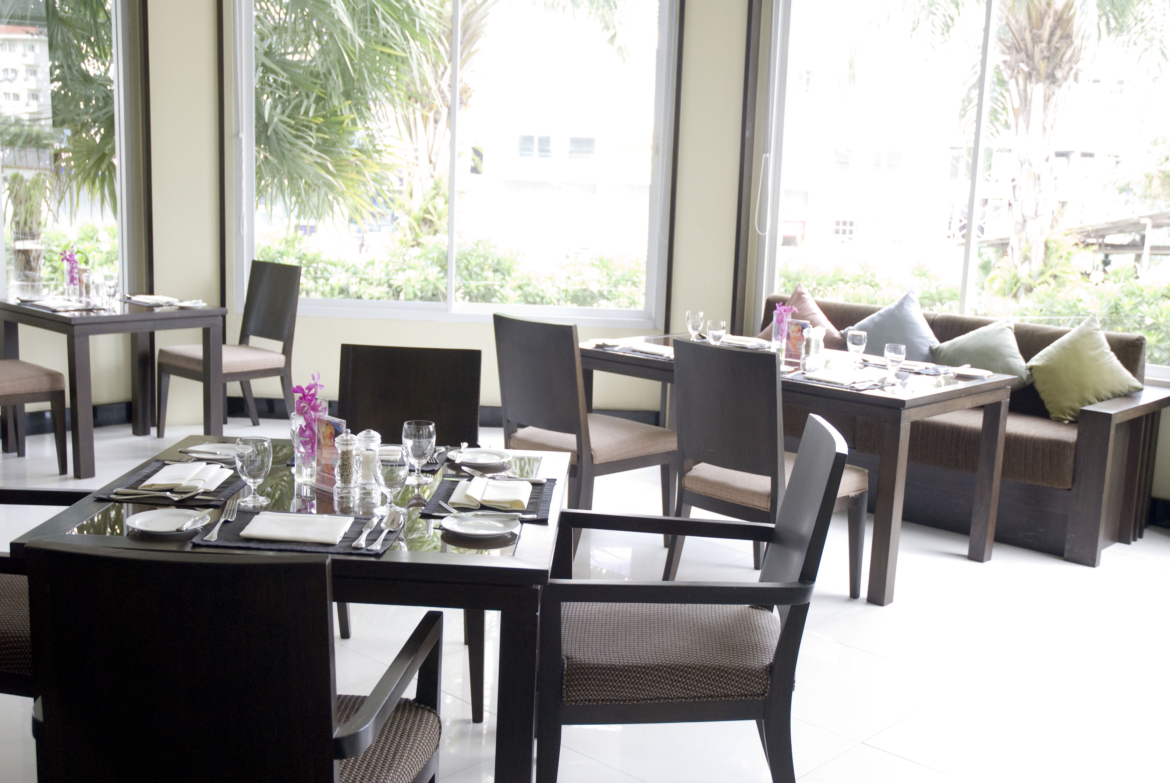 A dining area with tables set for two, chairs, and a sofa.