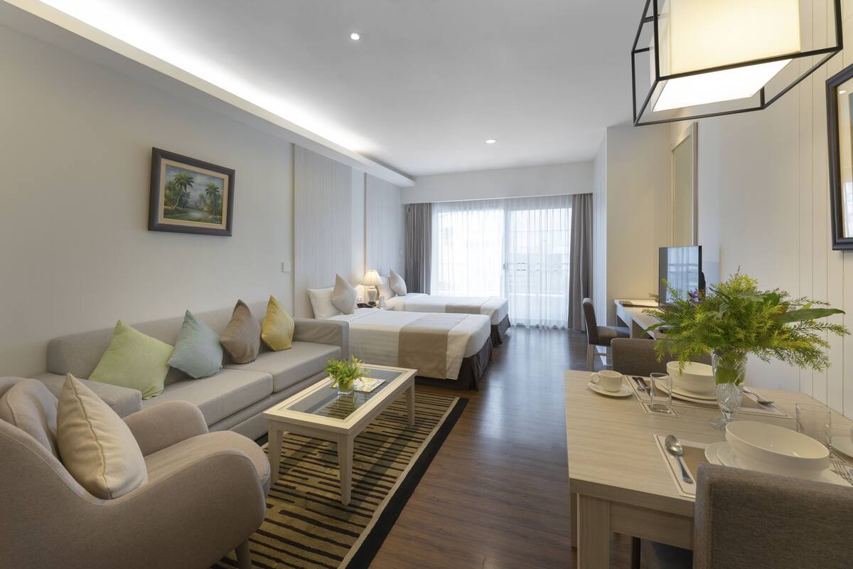 A modern hotel room with a sofa, a dining table, a bed, and a large window.