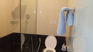 Un baño con cabina de ducha de vidrio, inodoro, bidé y un cubo de basura.