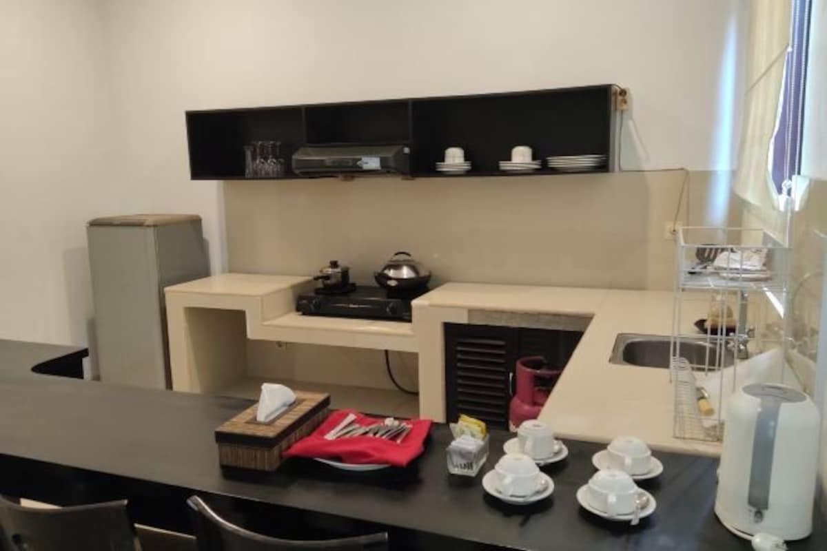A compact kitchen with a sink, a coffee machine, and a microwave. There are shelves above the counter holding plates and glasses.