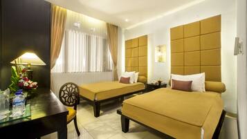 A hotel room with two beds, a desk with a lamp, a chair, and a window with curtains.
