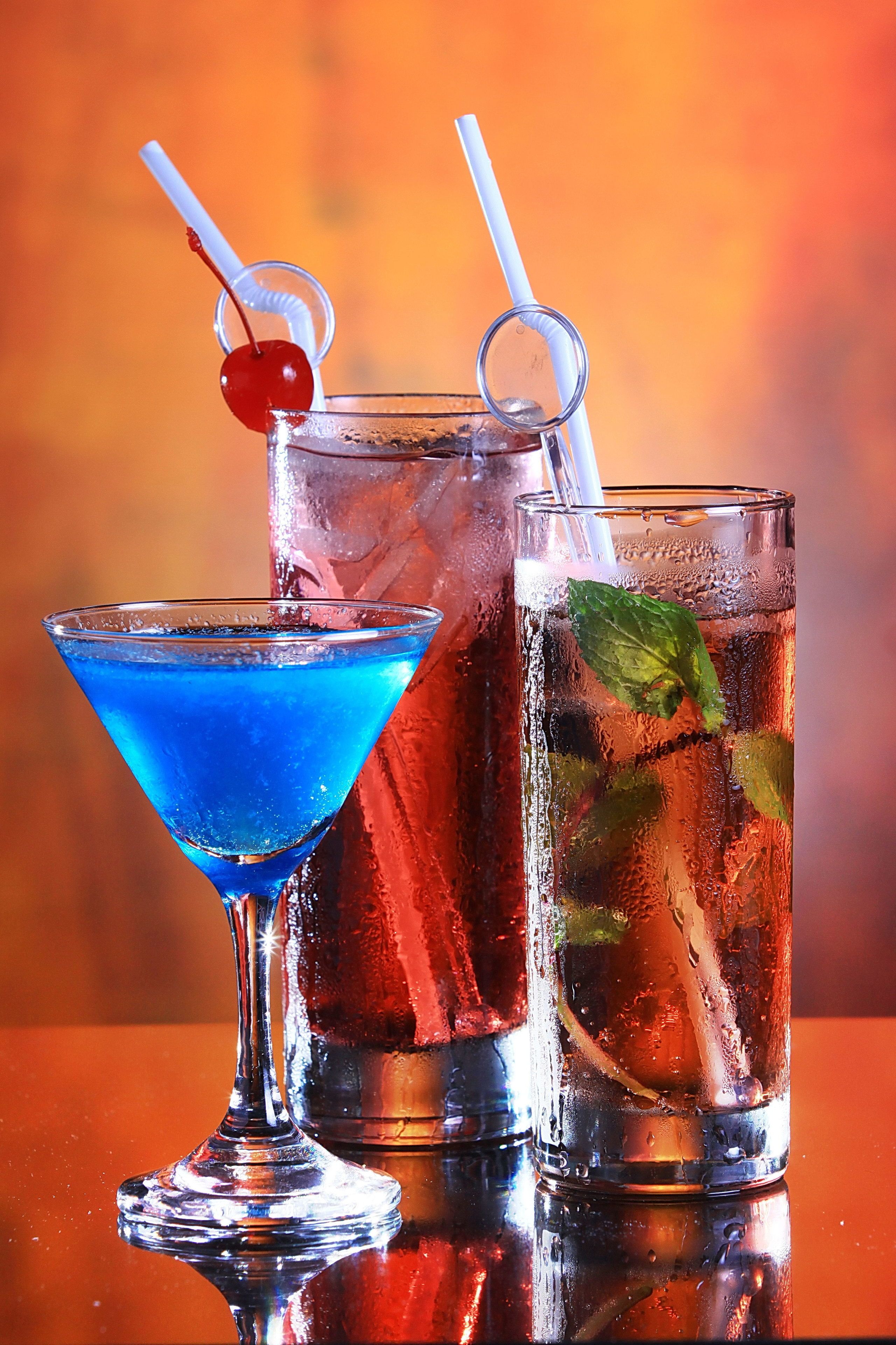 Three glasses of beverages with straws, one with a cherry garnish.