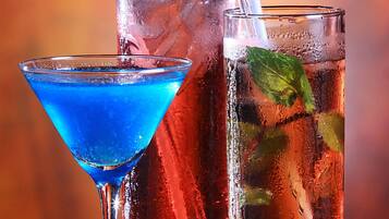 Three glasses of beverages with straws, one with a cherry garnish.