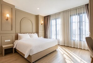 Una habitación de hotel con una cama grande, mesitas de noche, una silla y un ventanal con cortinas.