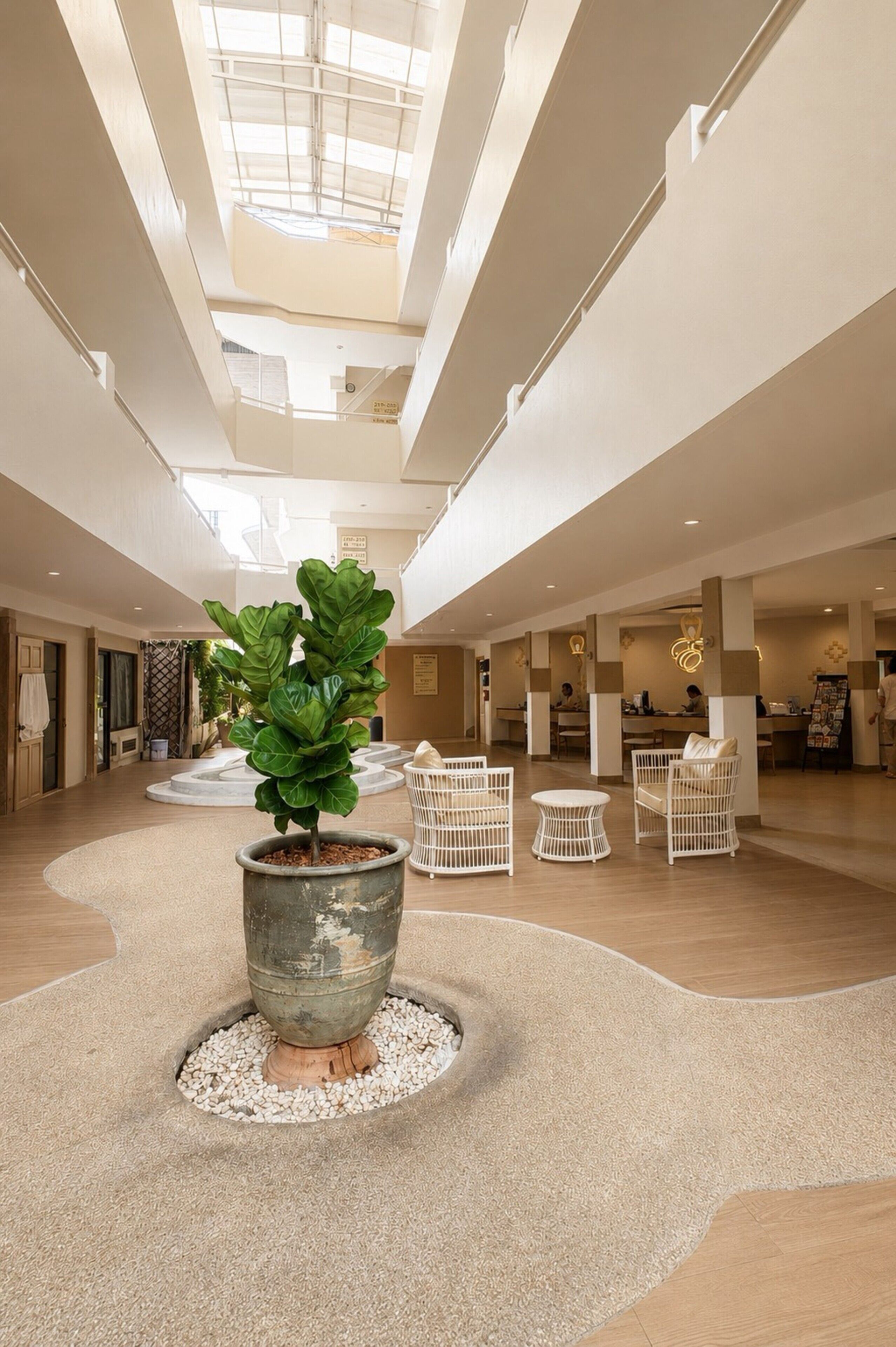 A spacious lobby with a central potted plant, seating areas, and a high ceiling with skylights.