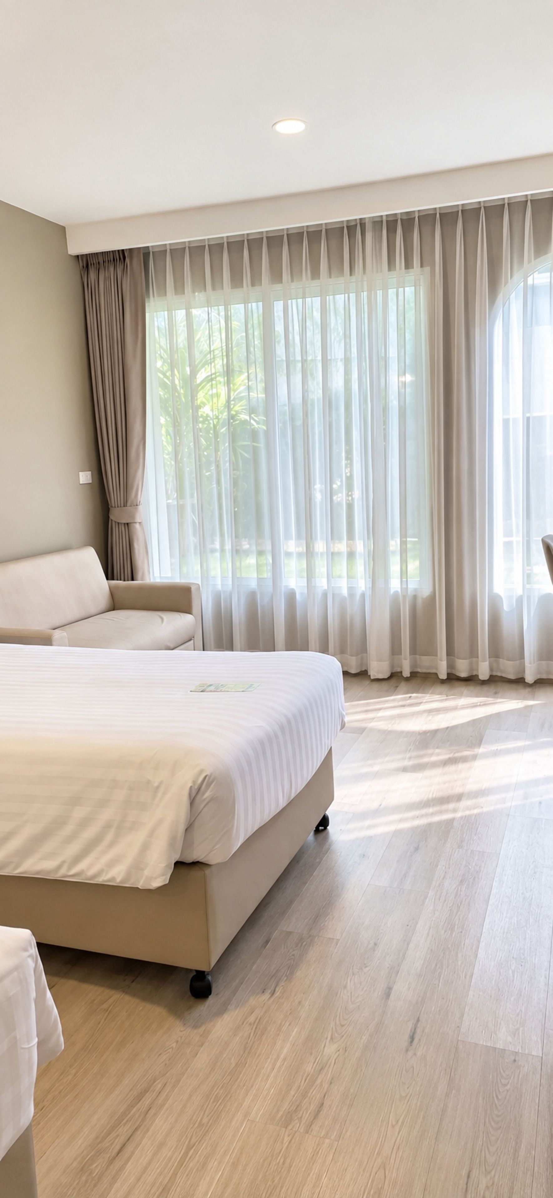 A modern bedroom with a large bed, a chair, and a window with sheer curtains.