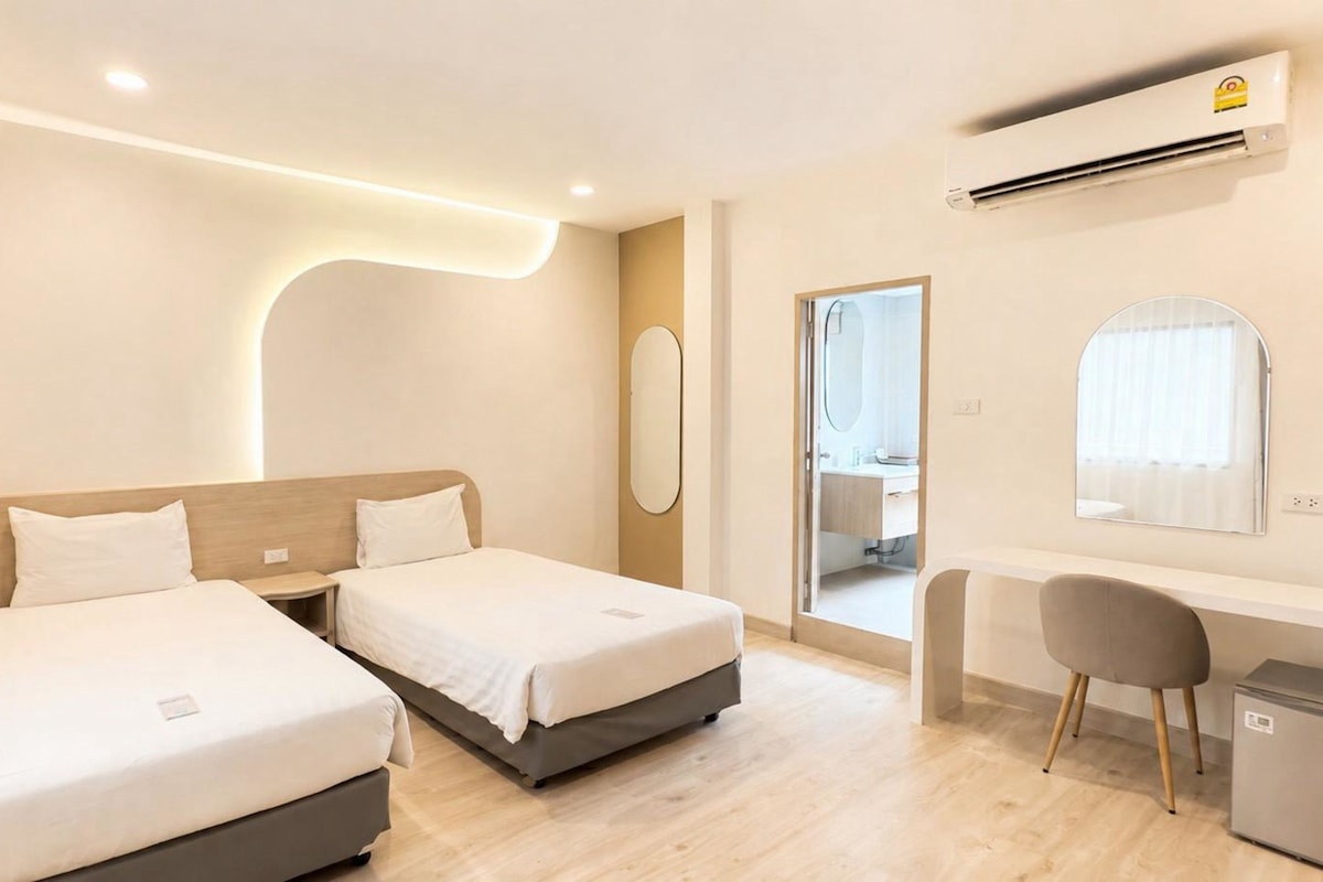 A hotel room with two beds, a desk, a chair, a mirror, and an air conditioning unit.