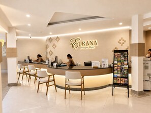 Un comptoir d’accueil d’hôtel au design moderne, une enseigne indiquant l’emplacement de l’hôtel-boutique et un panneau d’information touristique.