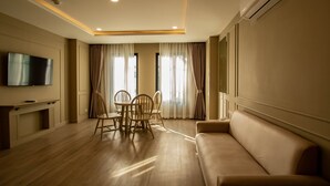 A modern living room with a flat-screen TV, a sofa, a dining table with chairs, and large windows with curtains.