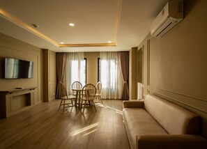Una sala de estar moderna con un televisor de pantalla plana, un sofá, una mesa de comedor con sillas y ventanas grandes con cortinas.