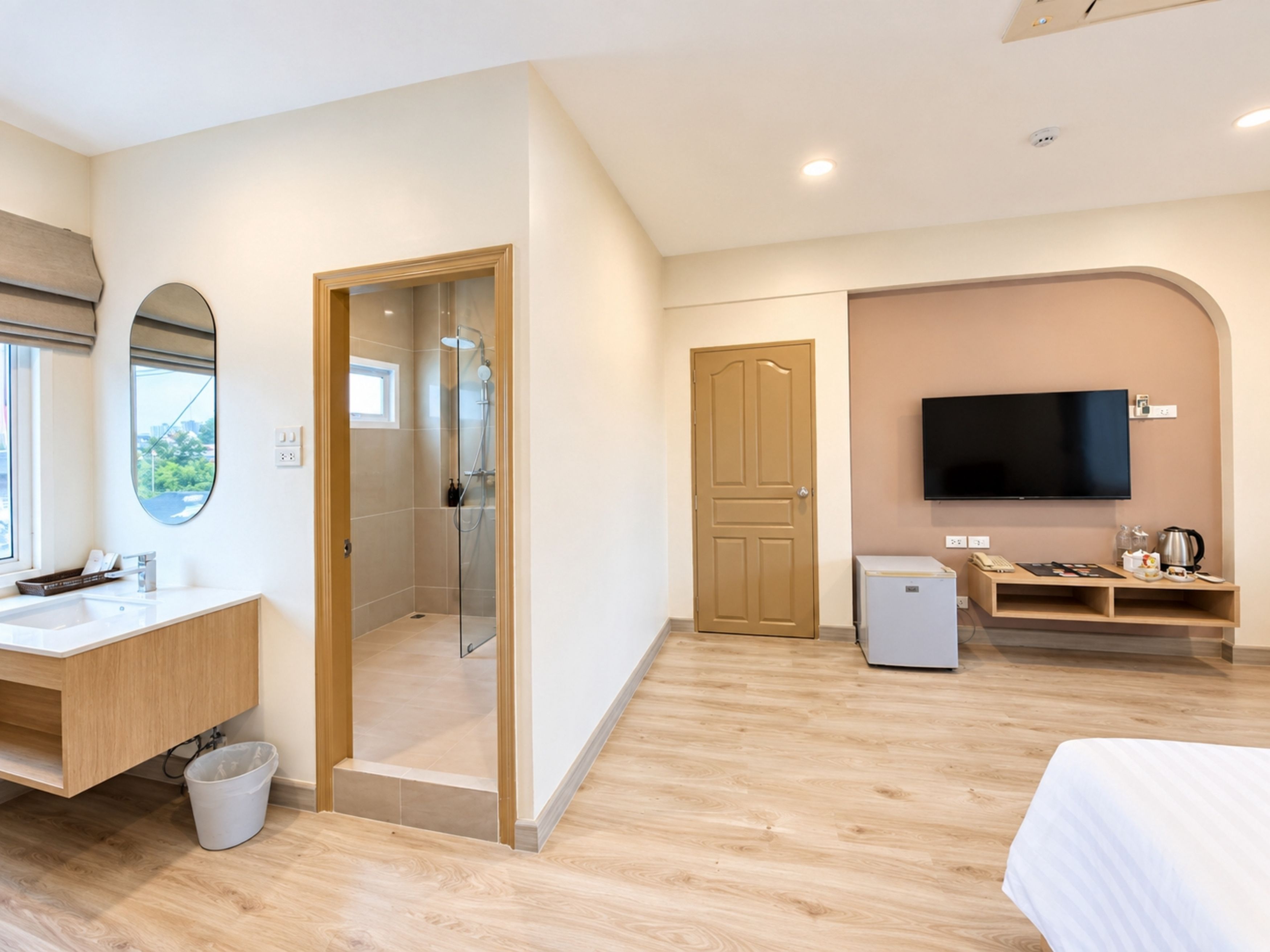 A modern hotel room with a shower, a TV, a small kitchenette, and a large window.
