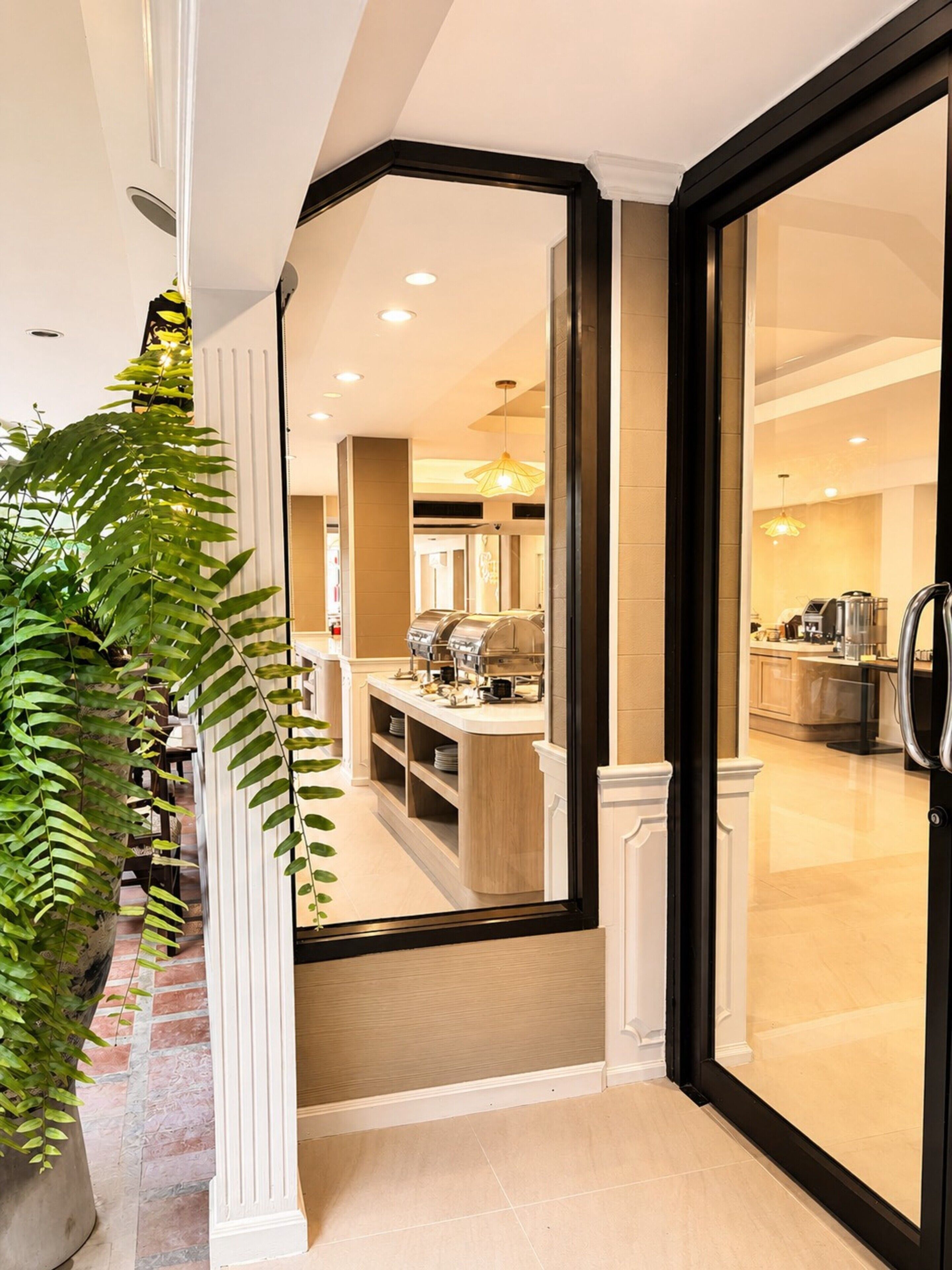A modern hotel interior with a reception desk, a coffee machine, and a kitchen area visible through a glass door.