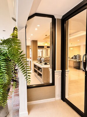 L'intérieur moderne d'un hôtel, avec un comptoir d'accueil, une machine à café et un coin cuisine visible à travers une porte vitrée.