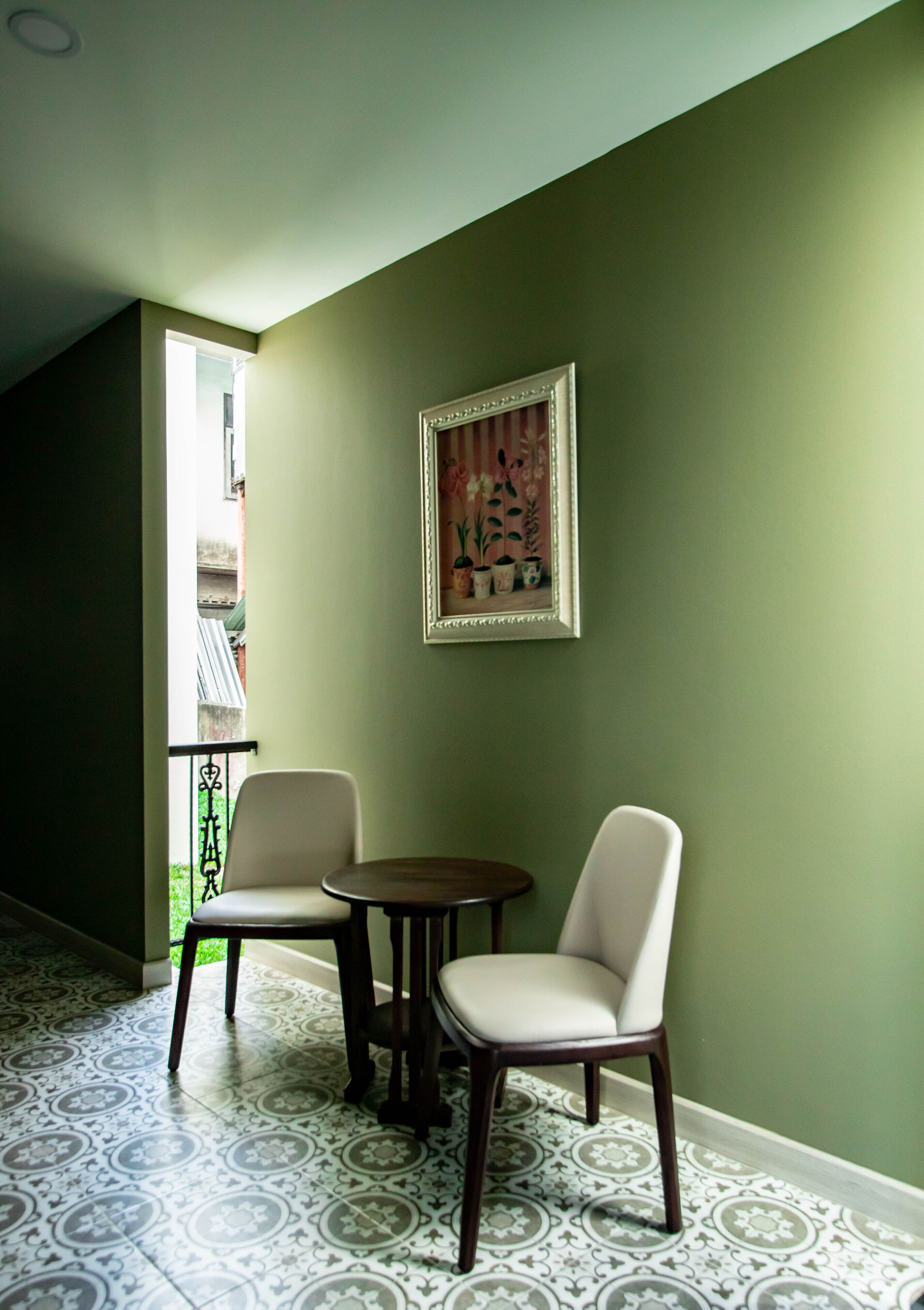 A room with two chairs and a small table, a framed picture on the wall, and patterned floor tiles.