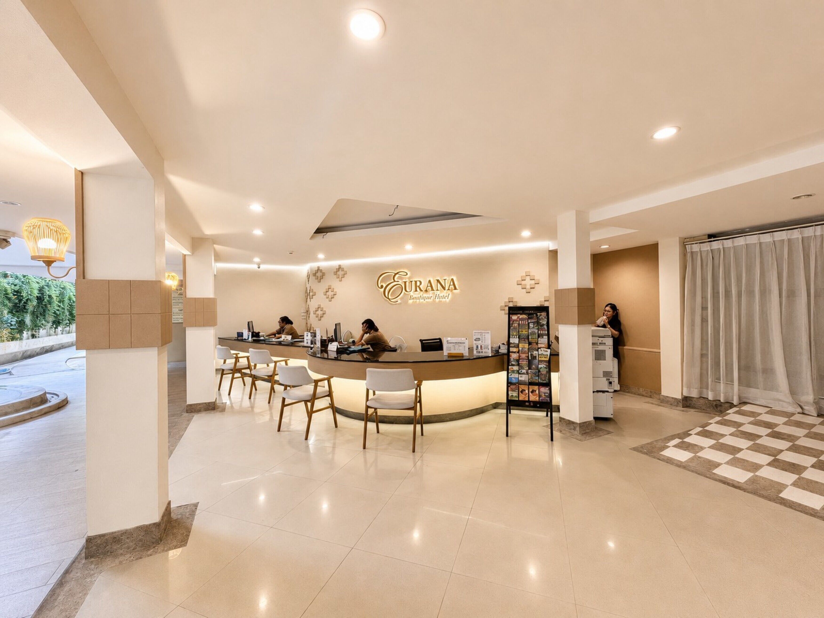 Zona de recepción de un hotel, con un mostrador de recepción, varias sillas y una mesa de registro.