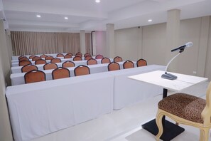 Un salón de conferencias con filas de mesas blancas y sillas anaranjadas, un atril para micrófono y una sola silla de estampado de leopardo.