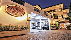 The exterior of the Curand Boutique Hotel with a well-lit entrance, a covered parking area, and a multi-story building with balconies.