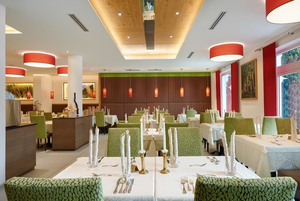 A restaurant with green upholstered chairs, white tablecloths, and red pendant lights.