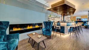 A modern bar area with a fireplace, bar stools, and a seating area with a table and chairs. - Anatol (Merano)