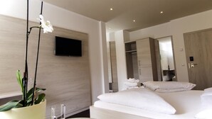 A modern hotel room with a large bed, a flat-screen TV mounted on the wall, a wooden wardrobe, and a potted plant. - Anatol (Merano)