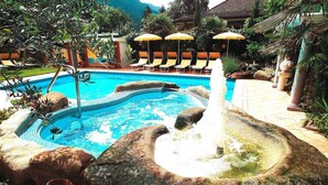 A pool with a water fountain, lounge chairs, and umbrellas. - Anatol (Merano)
