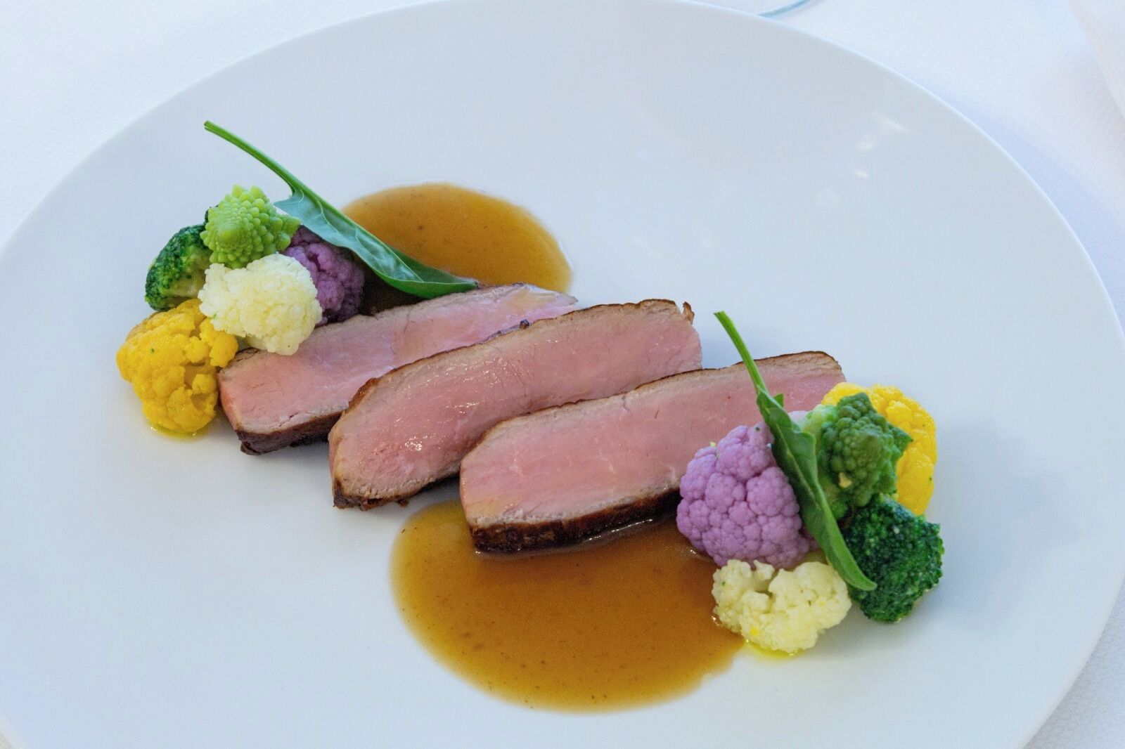 Ein Teller mit geschnittenem Fleisch, Blumenkohl und Soße.