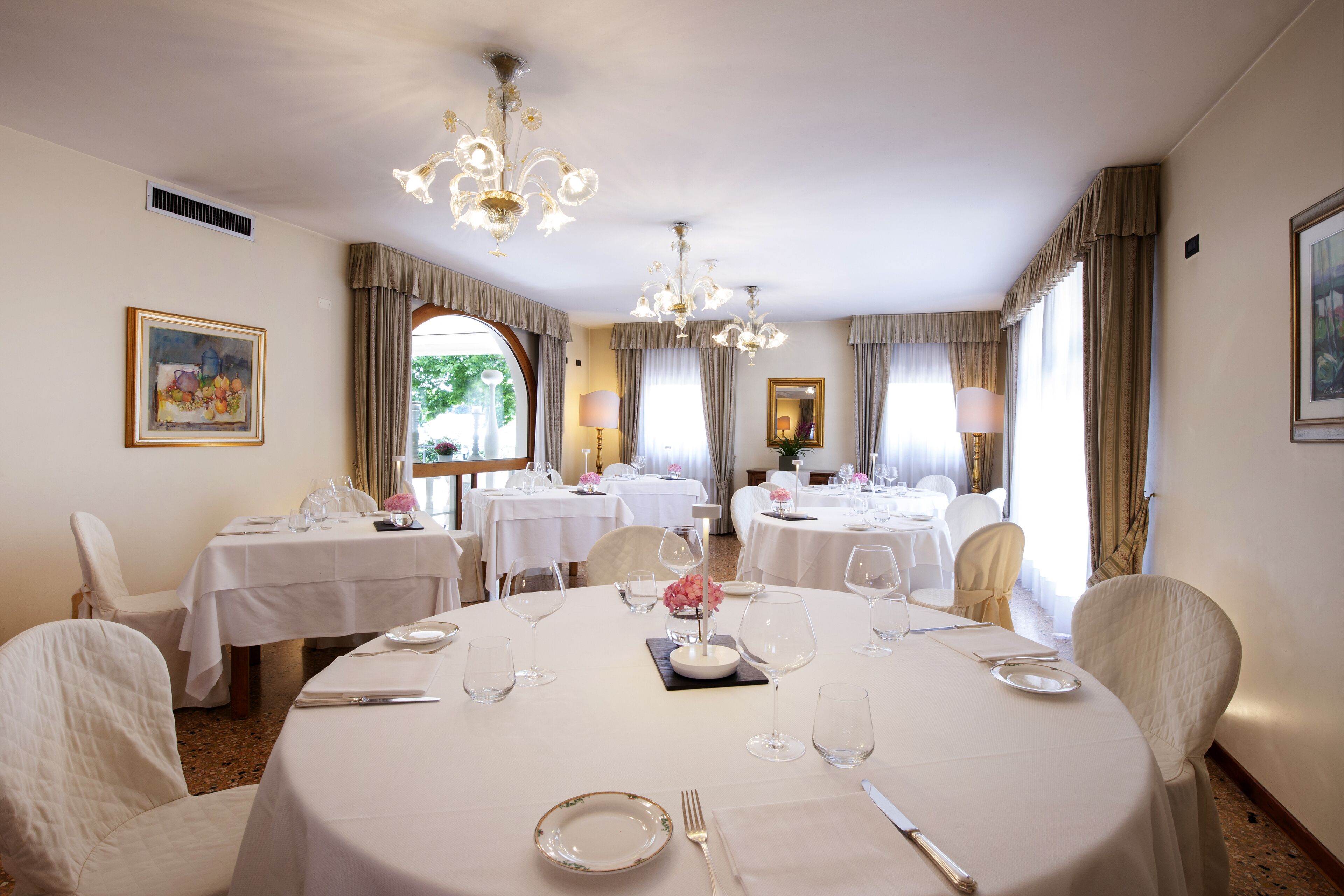 Zona pranzo con tavoli rotondi, tovaglie bianche e lampadari.