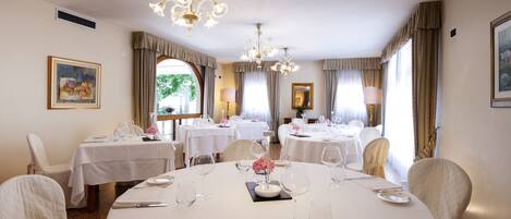 A dining area with round tables, white tablecloths, and chandeliers.