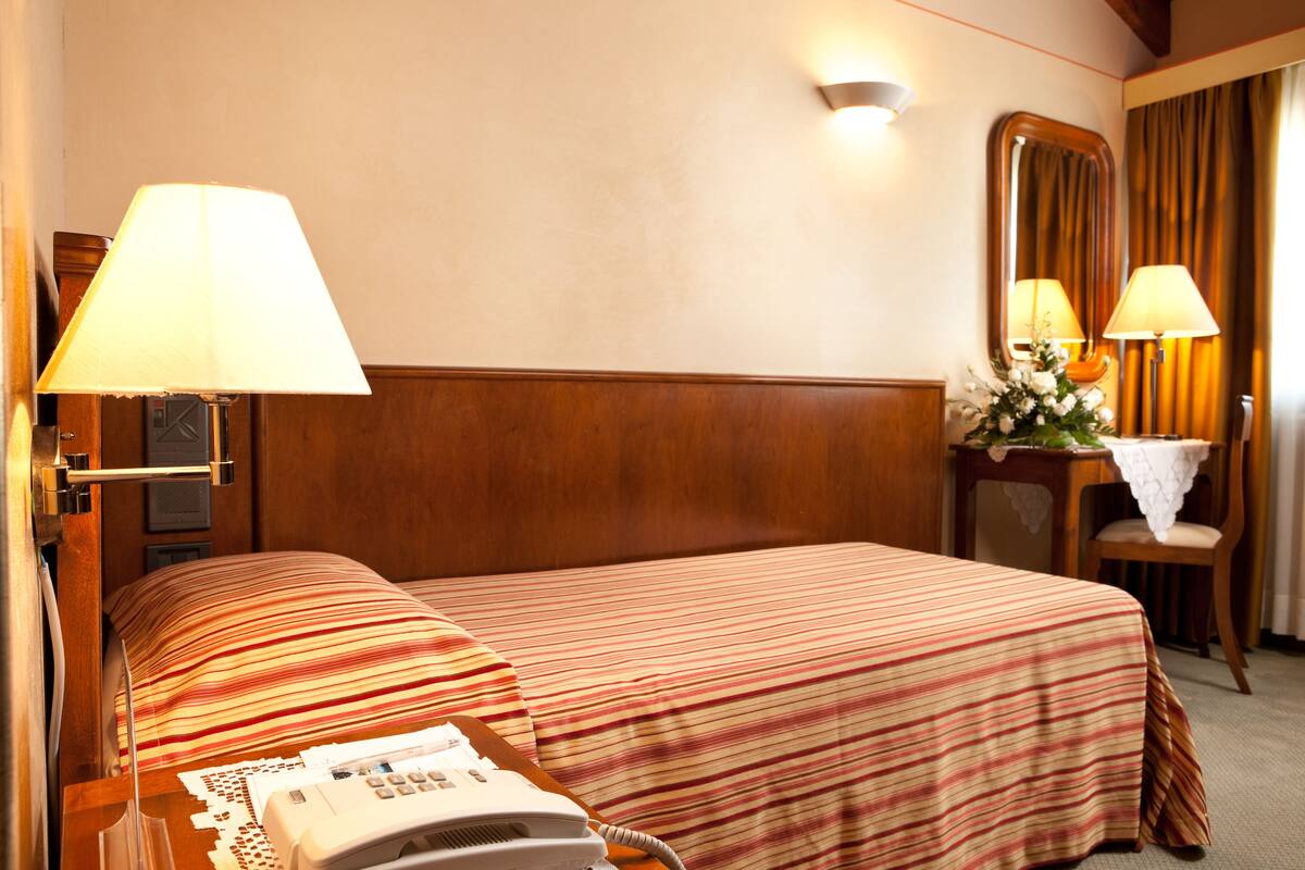 A hotel room with two beds, a telephone, a mirror, and a small table with a vase of flowers.