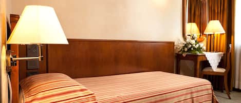 A hotel room with two beds, a telephone, a mirror, and a small table with a vase of flowers.