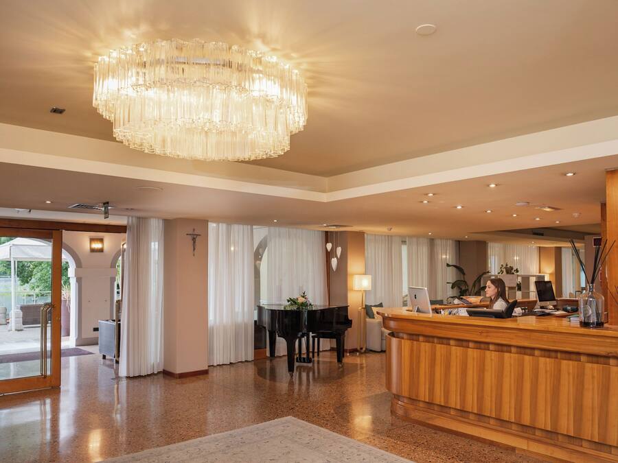 Eine Hotelhalle mit einem prächtigen Kronleuchter, einer Rezeption, einem Klavier und einer Sitzecke mit Blick ins Freie.