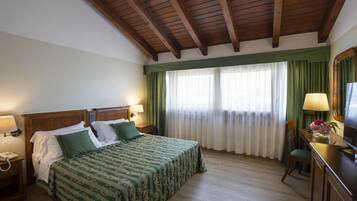 A hotel room with a wooden ceiling, a large bed with green bedding, a desk with a lamp, and a television.