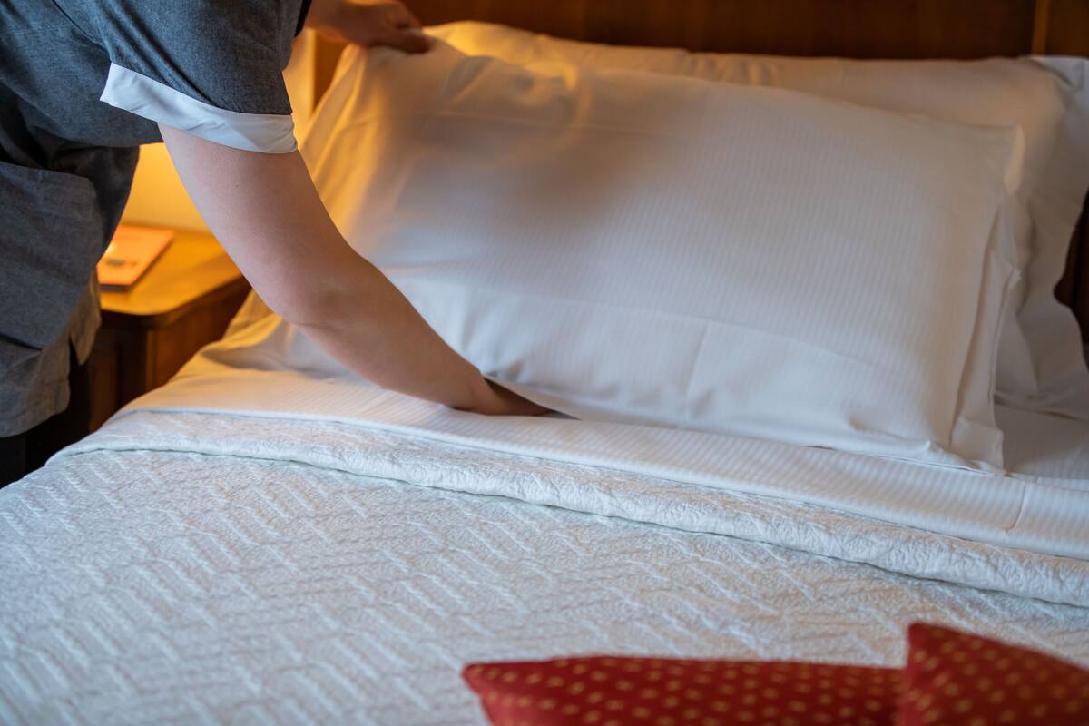 A neatly made bed with white bedding and a red pillow.