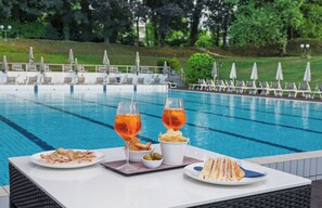Une table dressée au bord de la piscine, avec deux verres de boisson à l’orange et des assiettes de nourriture.