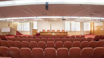 A conference room with rows of chairs, a podium, and a stage with curtains.