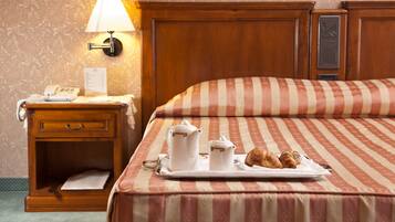 Habitación de hotel con cama, mesita de noche con lámpara, bandeja con artículos de desayuno y teléfono instalado en la pared.