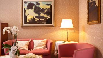 Une pièce avec un canapé rose, un fauteuil assorti, une table sur laquelle est posé un vase rempli d’orchidées blanches, un tableau encadré représentant un coucher de soleil et une lampe sur une table d’appoint.