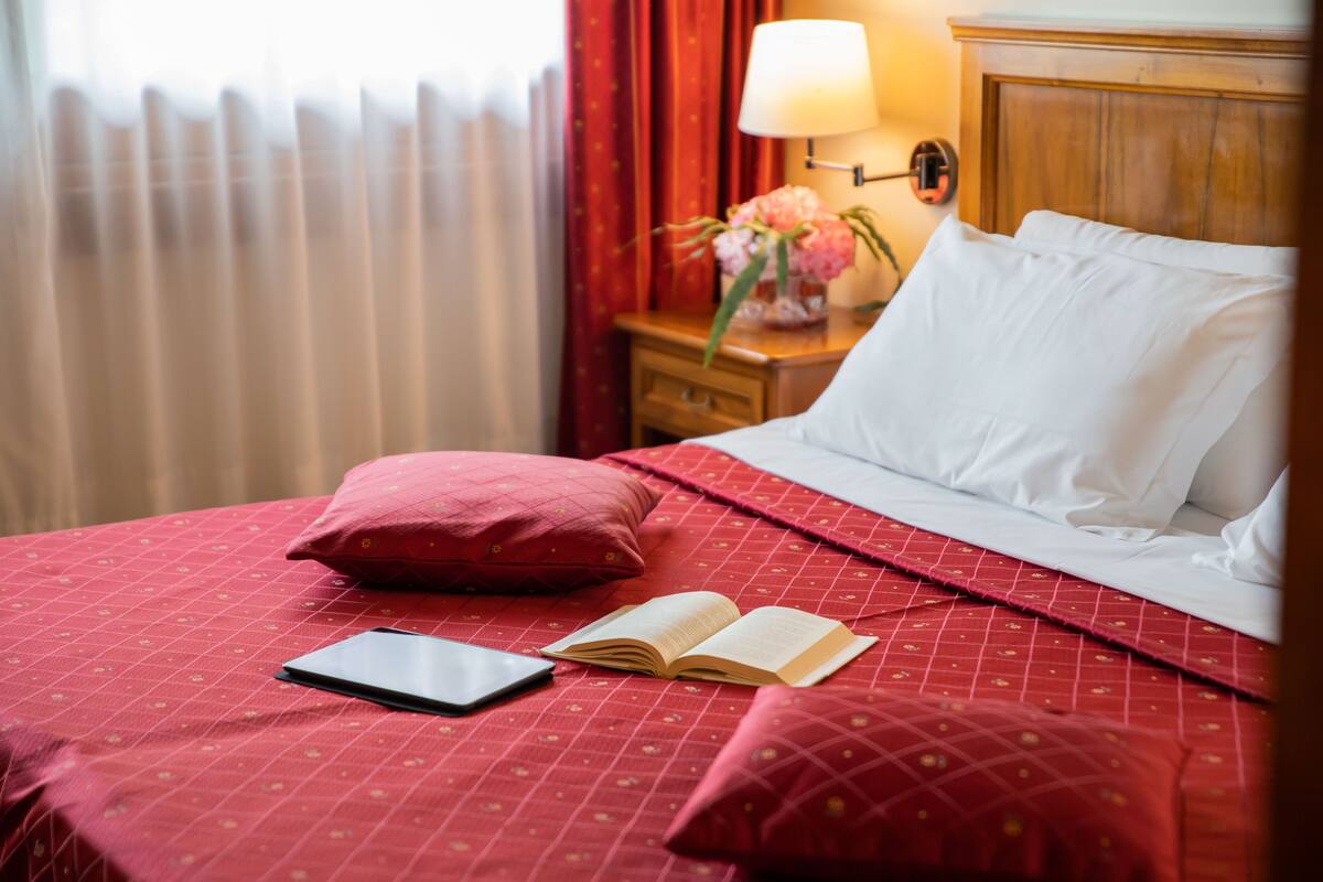 A neatly made bed with a red bedspread, a pillow, and an open book.